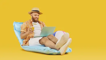 Positive man enjoys his work life, relaxing on an inflatable mattress with a laptop and mocktail, against an orange background, embracing the essence of fun and relaxation.