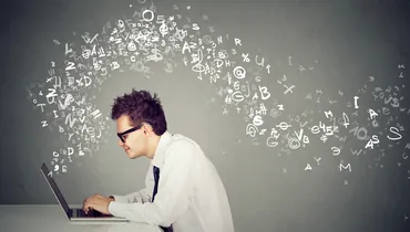 young man typing resume on computer with words and letters flying over his head