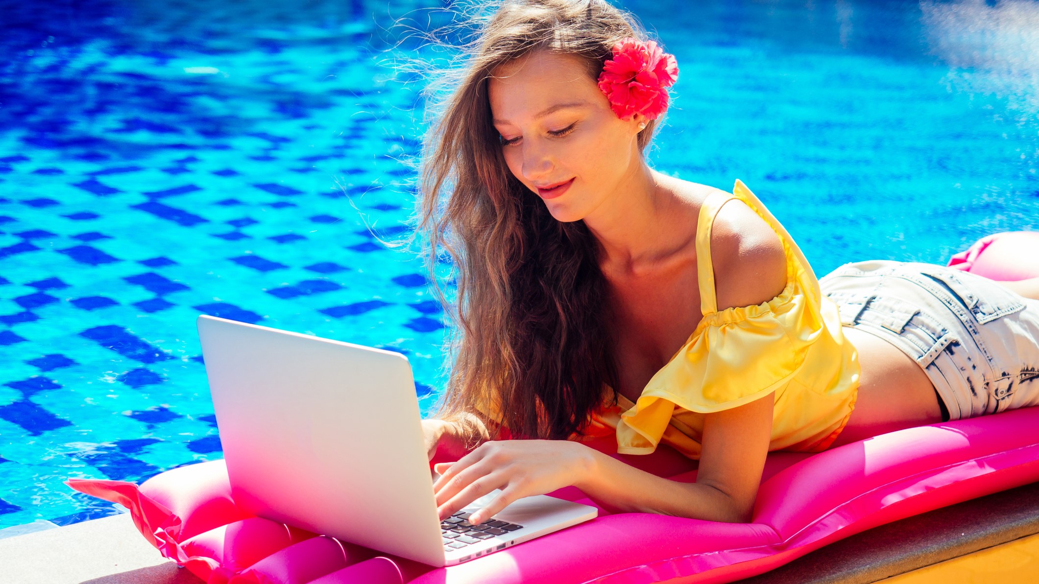 Remote job dream job. Young woman sitting by a pool  in the sun working on her computer
